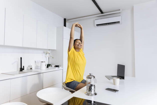 IMAGO Creative: Business, Innovative Technologie-Lösungen Happy woman stretching in kitchen taking a break fron freelance work model released, Symbolfoto property released, SIF00480