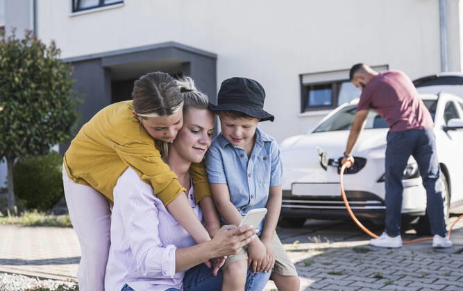IMAGO Creative: Business, Innovative Technologie-Lösungen Mother and children checking smartphone while father is charging electric car model released, Symbolfoto property released, UUF27090