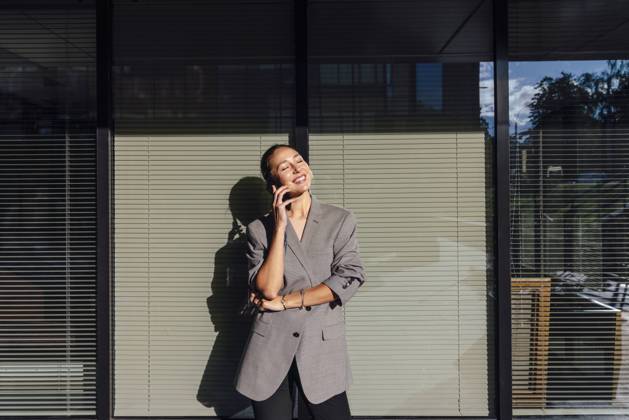 IMAGO Creative: Business, Innovative Technologie-Lösungen Smiling businesswoman with eyes closed talking on mobile phone in front of glass wall model released, Symbolfoto, VPIF07169