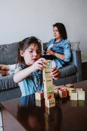 IMAGO Creative: Business - Work-Life Balance Concentrated young Latin American female freelancer sitting on sofa and working remotely on laptop near cute little daughter playing with wooden cube toys at home, Model released, Property released MarcosCastillo_LatinFamily_27 Copyright: xMarcosxCastillox MR