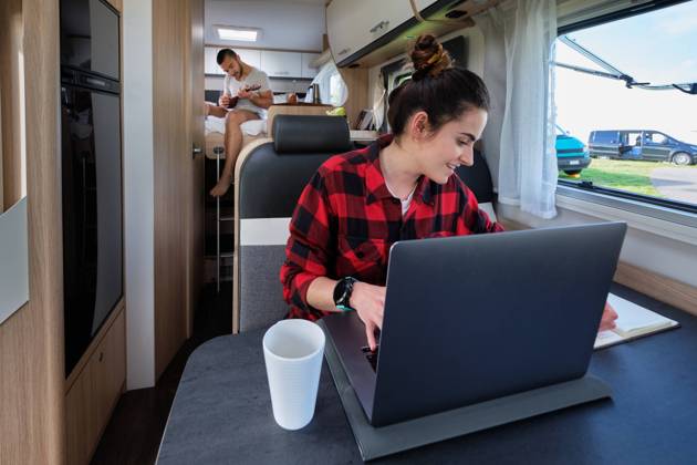 Content traveling female freelancer browsing laptop and taking notes in notebook while working remotely in camper on background of boyfriend, Model released Pempki_CamperCouple_14 Copyright: xIkerxZunigax MR