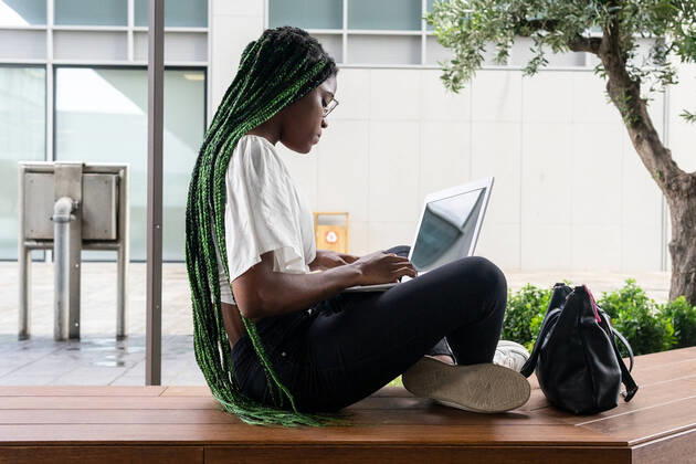 IMAGO Creative: Business - Work-Life Balance Side view of young African American female freelancer with long braided hair and in glasses sitting on wooden bench and browsing laptop in city downtown DavidMunoz_ID994_37337_025 Copyright: xDavidxMunozx Model Released