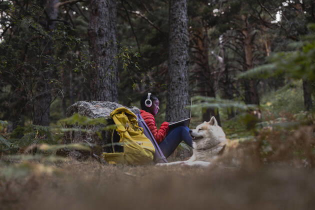 IMAGO Creative: Business - Work-Life Balance Woman wearing wireless headphones using laptop in forest model released, Symbolfoto property released, JCCMF07450