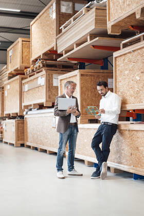 IMAGO Creative: Business, Inflation und Lieferketten Businessman holding laptop talking to colleague standing in warehouse model released, Symbolfoto property released, JOSEF13838