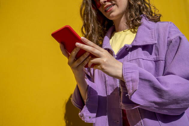 IMAGO Creative: Business, Innovative Technologie-Lösungen Woman wearing jacket using smart phone near yellow wall model released, Symbolfoto, VPIF07344