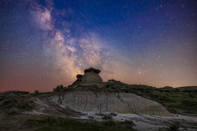 The galactic centre area in Sagittarius (at left) and Scorpius (at right) low in the south on a summer night at Dinosaur Provincial Park, Alberta. This was June 30 July 1, 2022. Being just 10 days after summer solstice and at latitude +50Â° North, the sky even to the south still has a blue tint from all-night twilight. I made no attempt to neutralize the sky colouration. In addition, some haze from smoke discoloured the sky and reduced transparency and contrast low in the sky. Many of the nebulas and star clusters in this part of the Milky Way are visible, many of them showpiece Messier objects for binoculars and telescopes. The colourful area around the star Rho Ophiuchi above Antares is at right, though muted here by the smoke and haze. Copyright: xAlanxDyerx ADY-NOV-22-71