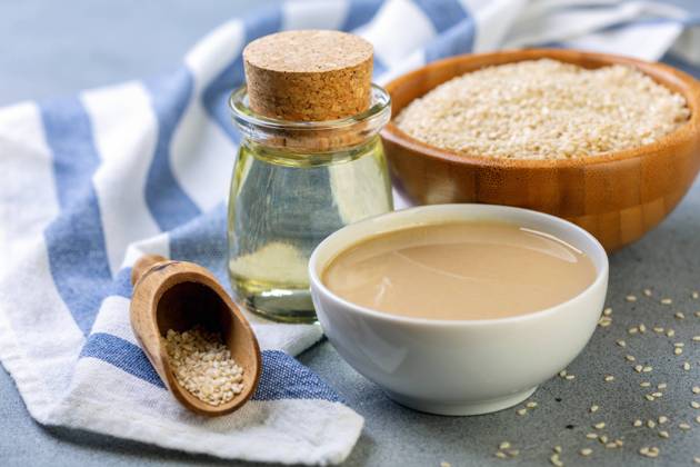 Bottled sesame oil, tahini and white sesame seeds. Cold pressed sesame oil from white sesame, tahini and sesame seeds in wooden bowl on grey textured background, selective focus. Copyright: xZoonar.com MarinaxSaprunovax 13304015
