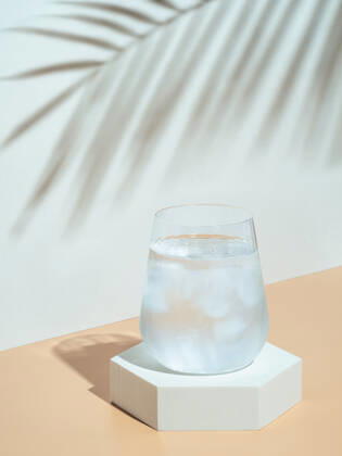 Modern still life with cold water glass Cold water with ice in tumbler glass on hexagon pedestal. Mockup for drink in fashion trendy style with tropical leaf shadow. Modern still life with glass. Copy space. Health, beverage, summer concept Copyright: xZoonar.com OlgaxSergeevax 15985952