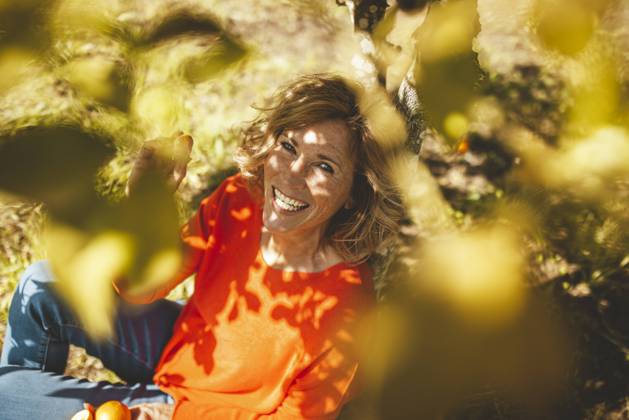 Happy mature woman sitting with orange fruits under tree model released, Symbolfoto property released, JOSEF15597