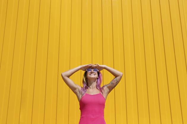 IMAGO Creative, Lifestyle, Barbiecore Happy woman wearing pink dress shielding eyes in front of yellow wall model released, Symbolfoto property released, SYEF00111