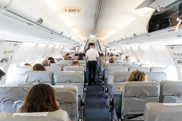 Interior of commercial airplane with passengers on their seats during flight. Interior of commercial airplane with unrecognizable passengers on their seats during flight. Steward in blue white uniform walking the aisle of commercial airplane. Copyright: xZoonar.com MatejxKastelicx 12698187