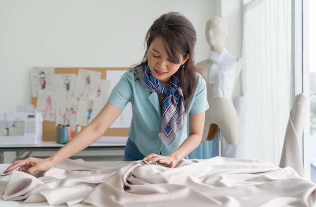  Fashion designer room. Young asian dressmaker in striped scarf spread out a piece of fine beige fabric on workbench preparing to create cloth pattern., Fashion designer room. Young asian dressmaker in striped scarf spread out a piece of fine beige fabric on workbench preparing to create cloth pattern., Fashion designer room. Young asian dressmaker in striped scarf spread out a piece of fine beige fabric on workbench preparing to create cloth pattern. model released, Symbolfoto property released , 11.12.2022, Copyright: xchadchaix Panthermedia33208887.jpg