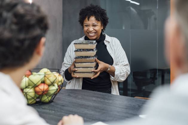 Cheerful young woman with lunch boxes standing by table in office model released, Symbolfoto property released, VPIF07749