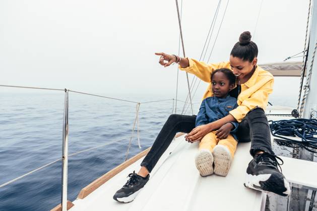 Full body of happy African American mother in casual clothes sitting on yacht and pointing away while smiling and showing view to little son during weekend, Model released AlfonsoSaenz_ID12778_387425_012 Copyright: xAlfonsoxSaenzx MR