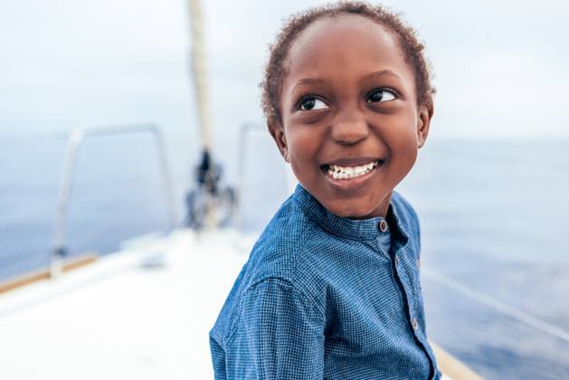 Creative Highlights Symbolbilder Positive African American boy in casual shirt smiling and looking away while sitting on yacht against sea, Model released AlfonsoSaenz_ID12778_387457_041 Copyright: xAlfonsoxSaenzx MR