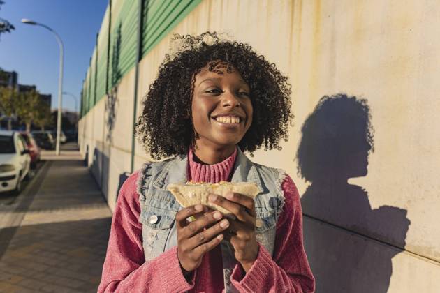 Happy woman holding sandwich standing at footpath model released, Symbolfoto, JCCMF09123