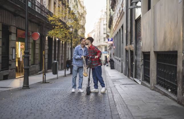 IMAGO Creative, Urban Lifestyle Happy gay couple kissing with electric push scooter amidst buildings model released, Symbolfoto property released, JCCMF09174