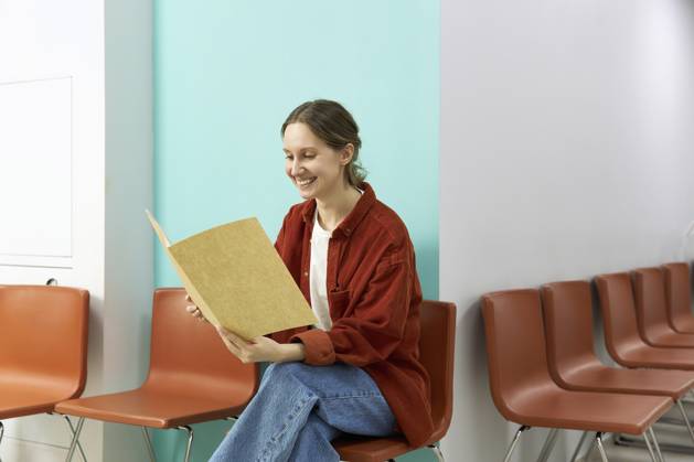 Happy woman reading medical results sitting on chair at clinic model released, Symbolfoto property released, SANF00037