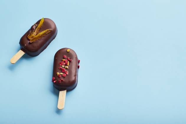 Mousse dessert with fruit flavors in the form of popsicle ice cream on blue background. Mousse dessert with fruit flavors in the form of popsicle ice cream covered with dark chocolate on blue background. Copyright: xZoonar.com BurakovaxIrinax 18196165
