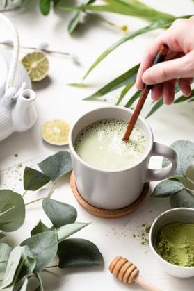 RECORD DATE NOT STATED A vertical shot of Green tea latte with milk in a white cup with green leaves and wooden spoon *** einer hoch erschossen des Grün Tee latte mit Milch ÊIn einer weiß Tasse mit Grün verlässt und hölzern löffeln 201073