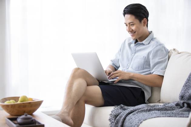 Happy young Chinese man using laptop in living room Beijing China Copyright: xLanexOateyx bji05860357