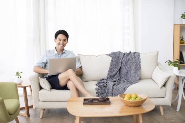 Happy young Chinese man using laptop in living room Beijing China Copyright: xLanexOateyx bji05860341