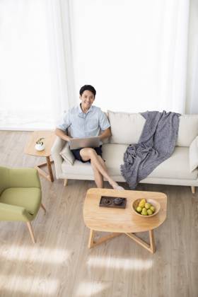 Happy young Chinese man using laptop in living room Beijing China Copyright: xLanexOateyx bji05860348