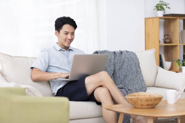 Happy young Chinese man using laptop in living room Beijing China Copyright: xLanexOateyx bji05860350