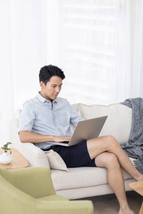 Happy young Chinese man using laptop in living room Beijing China Copyright: xLanexOateyx bji05860352