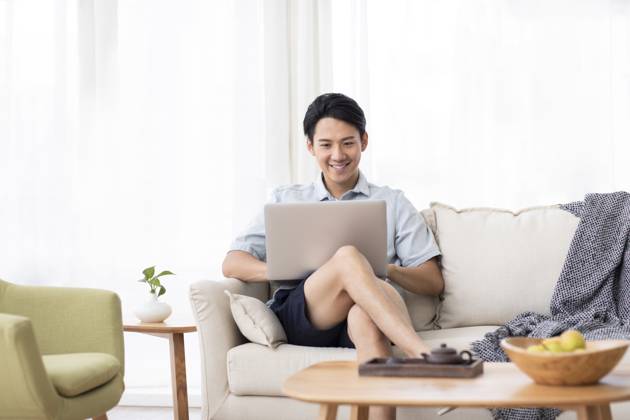 Happy young Chinese man using laptop in living room Beijing China Copyright: xLanexOateyx bji05860353