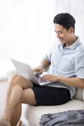 Happy young Chinese man using laptop in living room Beijing China Copyright: xLanexOateyx bji05860356