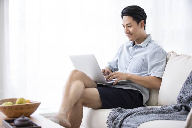 Happy young Chinese man using laptop in living room Beijing China Copyright: xLanexOateyx bji05860358