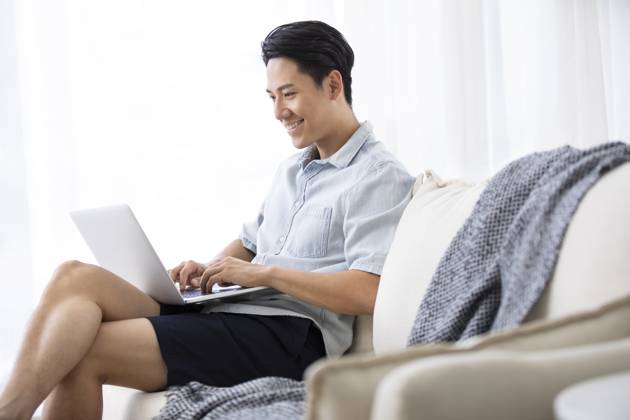 Happy young Chinese man using laptop in living room Beijing China Copyright: xLanexOateyx bji05860359