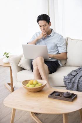 Happy young Chinese man using laptop in living room Beijing China Copyright: xLanexOateyx bji05860360