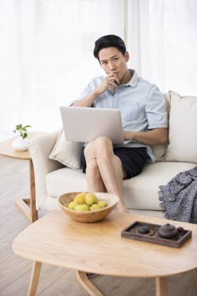 Happy young Chinese man using laptop in living room Beijing China Copyright: xLanexOateyx bji05860361