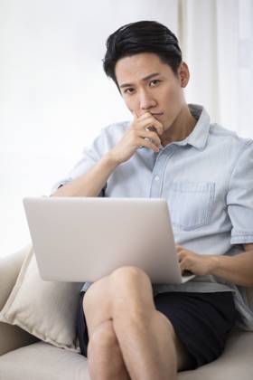 Happy young Chinese man using laptop in living room Beijing China Copyright: xLanexOateyx bji05860362