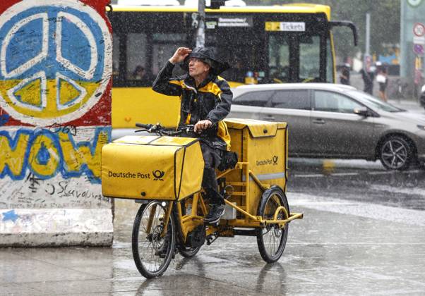 Rainy weather Berlin, 23 06 2023 A DHL mail carrier rides his e-bike over a sidewalk in heavy rain Heavy storms have moved over parts of Germany Berlin Berlin Germany