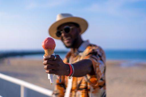 A shallow focus of a young handsome black man eating an ice cream cone at the beach *** einer seicht Fokus des einer Jung gutaussehenden Schwarz Mann essender An&Verkauf Eis Creme Kegel im der Strand 19751172 ,model released, Symbolfoto RECORD DATE NOT STATED
