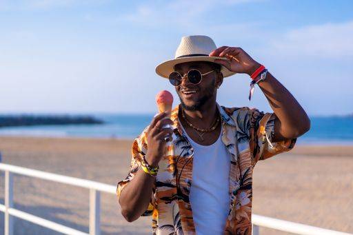 A shallow focus of a young handsome black man eating an ice cream cone at the beach *** einer seicht Fokus des einer Jung gutaussehenden Schwarz Mann essender An&Verkauf Eis Creme Kegel im der Strand 19751186 ,model released, Symbolfoto RECORD DATE NOT STATED