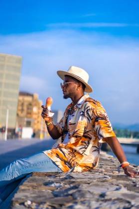 A shallow focus of a young handsome black man eating an ice cream cone at the beach *** einer seicht Fokus des einer Jung gutaussehenden Schwarz Mann essender An&Verkauf Eis Creme Kegel im der Strand 19751270 ,model released, Symbolfoto RECORD DATE NOT STATED