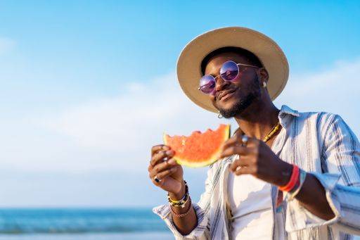 A shallow focus of a young handsome black man eating fresh watermelon at the beach *** einer seicht Fokus des einer Jung gutaussehenden Schwarz Mann essender Frisch Wassermelone im der Strand 19751282 ,model released, Symbolfoto RECORD DATE NOT STATED