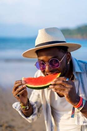 A shallow focus of a young handsome black man eating fresh watermelon at the beach *** einer seicht Fokus des einer Jung gutaussehenden Schwarz Mann essender Frisch Wassermelone im der Strand 19751284 ,model released, Symbolfoto RECORD DATE NOT STATED