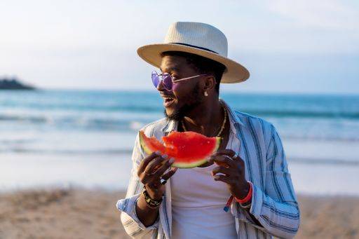 A shallow focus of a young handsome black man eating fresh watermelon at the beach *** einer seicht Fokus des einer Jung gutaussehenden Schwarz Mann essender Frisch Wassermelone im der Strand 19751289 ,model released, Symbolfoto RECORD DATE NOT STATED