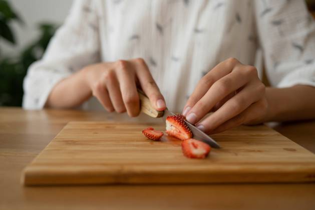 IMAGO Creative, Jahreszeit Sommer, Food, Marmelade kochen PR_ID15648_4255_Room.jpg, MR_ID15648_14434_MayaSolopova.jpg Crop anonymous female in white cloth sitting and cutting red strawberry on board over wooden table while making strawberry jam indoors, Property released MR LiliyaSolopova_ID15648_475515_011 Copyright: xLiliyaxSolopovax Model Released