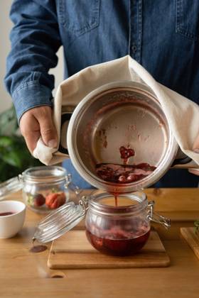 IMAGO Creative, Jahreszeit Sommer, Food, Marmelade kochen PR_ID15648_4255_Room.jpg, MR_ID15648_14436_KonstantinSolopov.jpg Crop anonymous person in casual clothes pouring hot strawberry jam into jar while standing at wooden table with bowl, Property released MR LiliyaSolopova_ID15648_475534_021 Copyright: xLiliyaxSolopovax Model Released