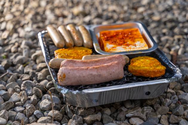Bavaria, Germany - 2 September 2023: Vegetarian Grilling, Bratwurst Vegan and Vegetarian on a disposable grill on pebbles next to a meadow. Meat and sausage substitutes