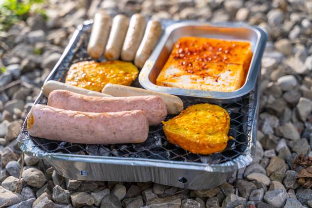 Bavaria, Germany - 2 September 2023: Vegetarian Grilling, Bratwurst Vegan and Vegetarian on a disposable grill on pebbles next to a meadow. Meat and sausage substitutes