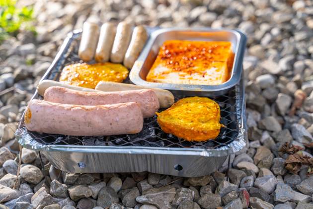 Bavaria, Germany - 2 September 2023: Vegetarian Grilling, Bratwurst Vegan and Vegetarian on a disposable grill on pebbles next to a meadow. Meat and sausage substitutes
