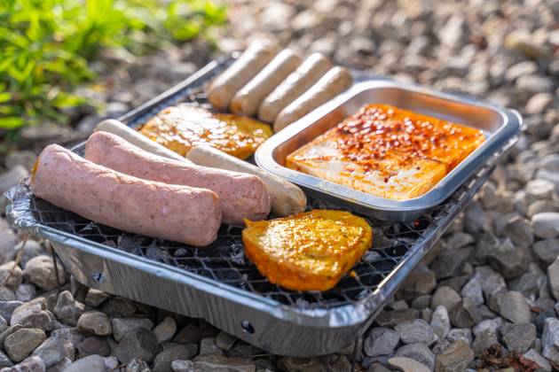 Bavaria, Germany - 2 September 2023: Vegetarian Grilling, Bratwurst Vegan and Vegetarian on a disposable grill on pebbles next to a meadow. Meat and sausage substitutes