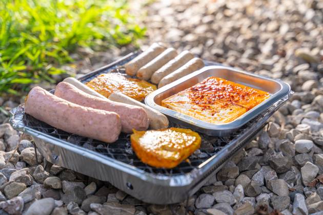 Bavaria, Germany - 2 September 2023: Vegetarian Grilling, Bratwurst Vegan and Vegetarian on a disposable grill on pebbles next to a meadow. Meat and sausage substitutes